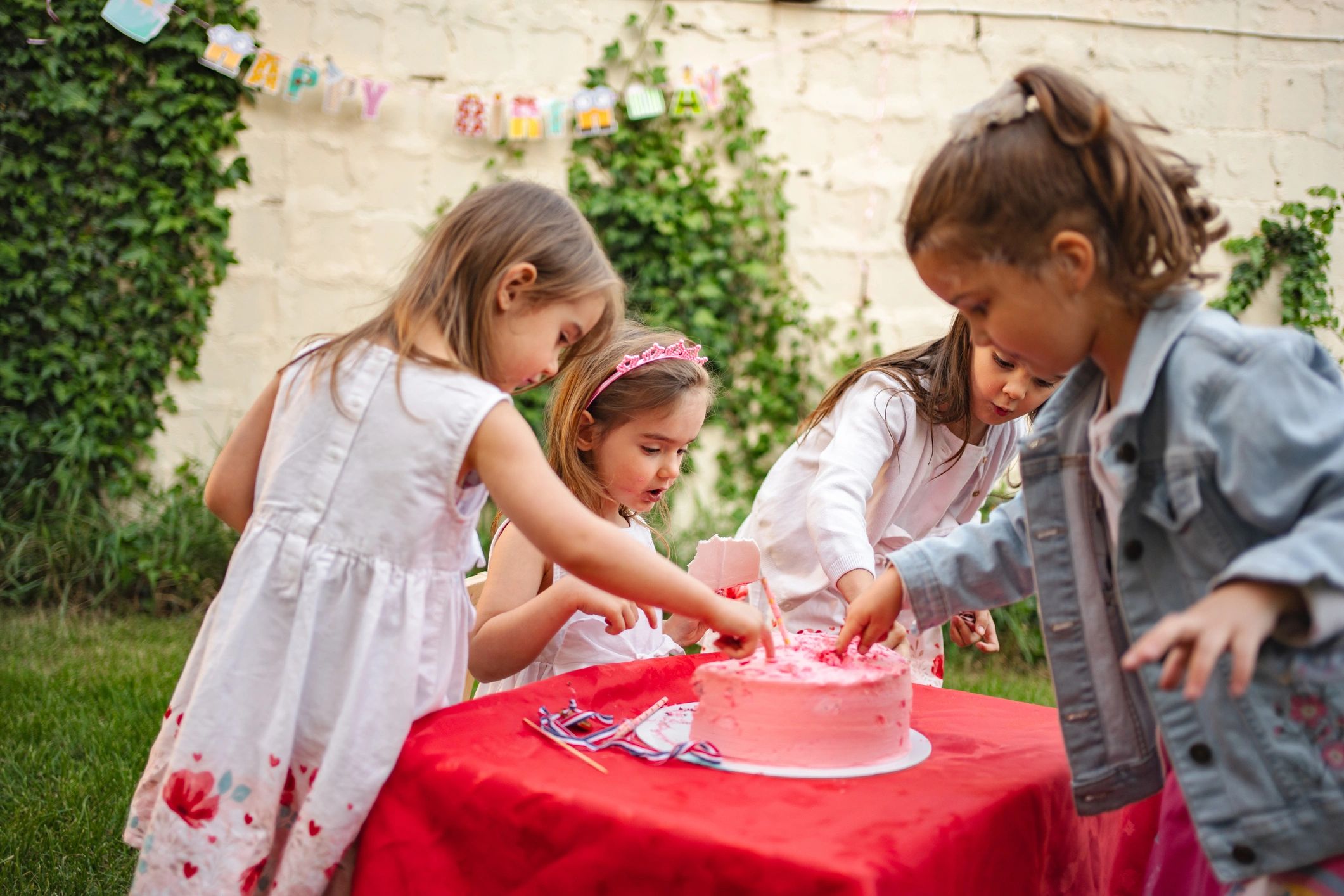 Four little girls tasting birthday cake at a party in the garden
