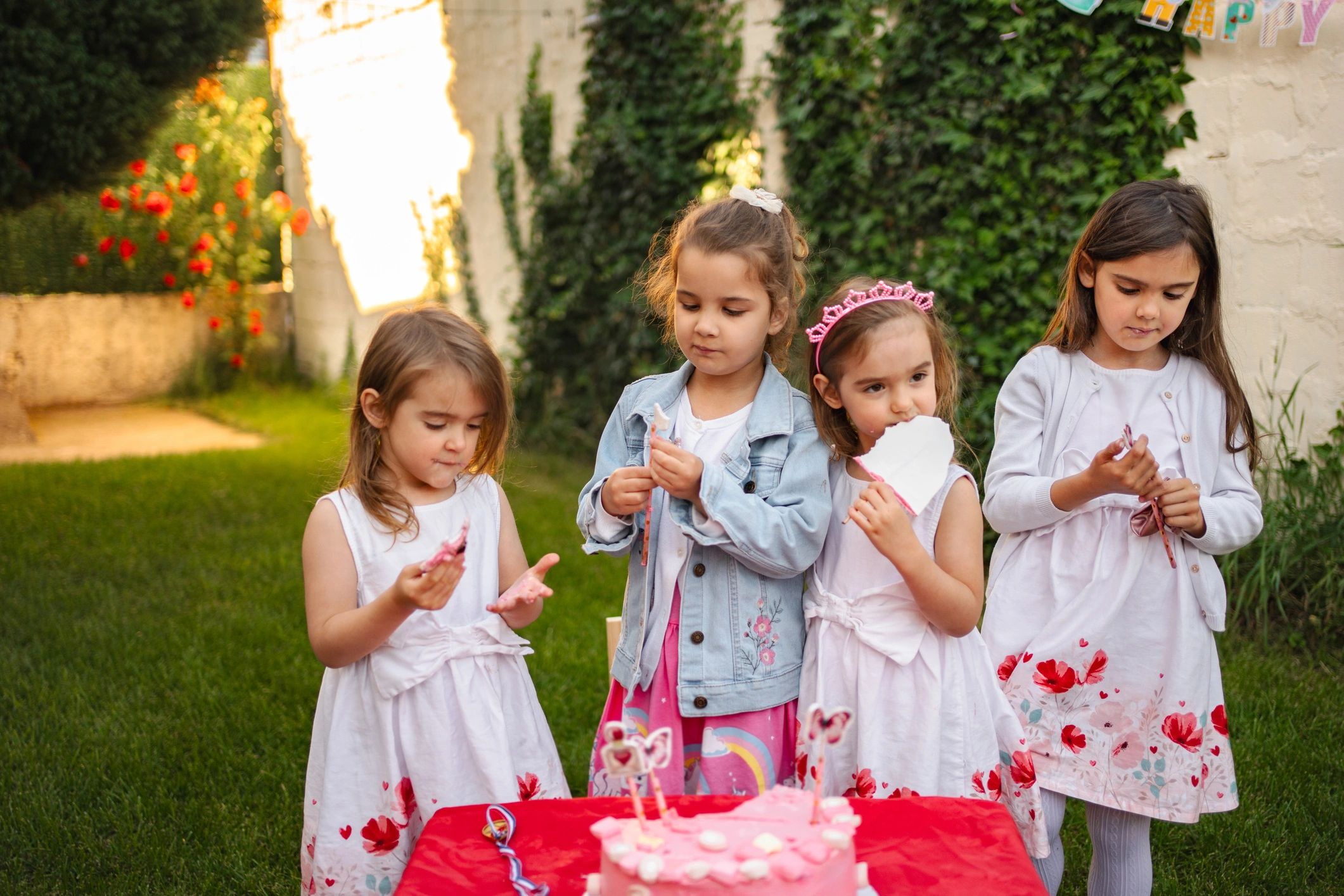 Four little girls eating cake at a birthday party in the garden