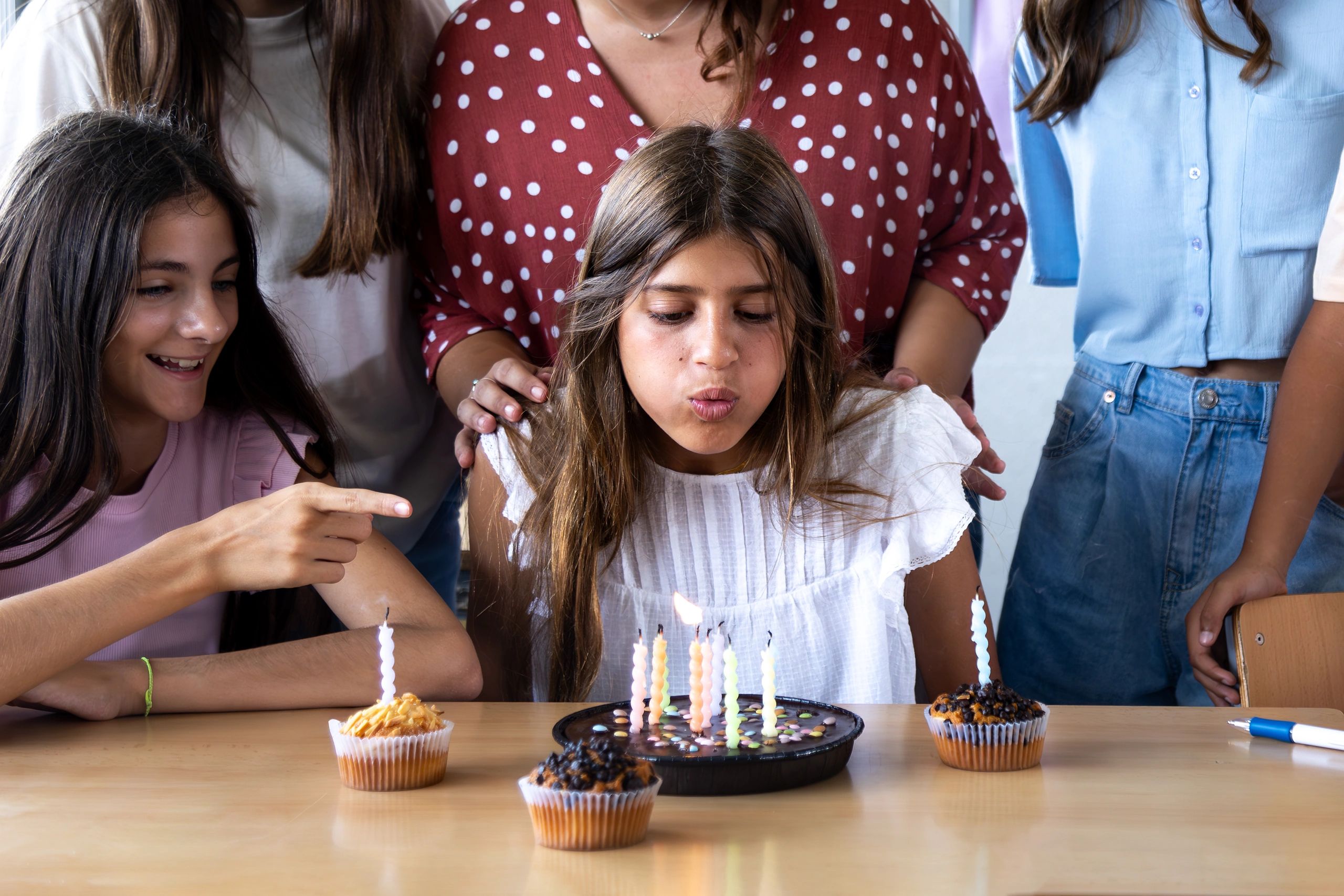Girl blowing out candles on birthday cake surrounded by family and friends